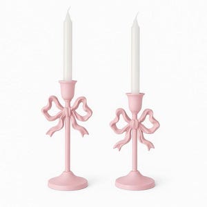Pode incluir: Dois castiçais rosa com um design de laço. Cada suporte tem uma base redonda, uma haste fina e um detalhe de laço. Velas brancas são inseridas no topo de cada suporte. O fundo é branco liso.