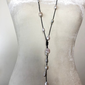 May include: A long black leather necklace with white pearl beads. The necklace has a tassel at the bottom and is adjustable.