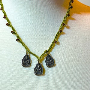 May include: A green crocheted necklace with brown beads and three small, gold-toned Buddha charms.