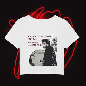 May include: White crop top featuring a graphic of a man, a disco ball, and text that reads "'CAUSE MY HEART BELONGS TO YOU I'LL RISK IT ALL FOR YOU". The design includes a CD graphic. The background is black with red neon accents.