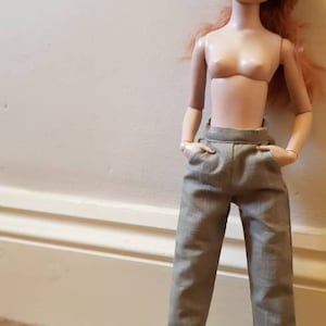 Op de afbeelding: Een pop die een lichtbruine broek draagt met een hoge taille.