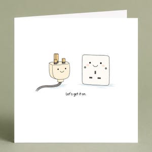 May include: A square greeting card featuring a cartoon illustration of a cream-colored electrical plug and a white wall outlet, both with smiling faces and pink cheeks. The text below the characters reads, Let's get it on. The design is simple.