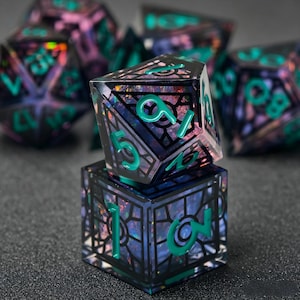 May include: A set of polyhedral dice featuring a dark, translucent resin base with iridescent, multi-colored flecks embedded inside. Each die has a black, cage-like frame overlay and bright teal, raised numerals for clear visibility.