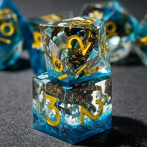 May include: A set of polyhedral dice made of clear blue resin, each containing a detailed bronze-colored octopus tentacle. The numbers are engraved in a bold, gold-colored font. The dice feature sharp edges and a transparent, aquatic appearance.