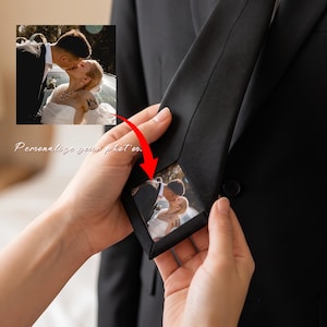 Può includere: Una cravatta nera a tinta unita con un inserto fotografico rettangolare nascosto sul retro, che mostra una coppia che si bacia. La cravatta è indossata sopra una giacca da abito nera. Il testo "Personalize your photos" è visibile in corsivo.
