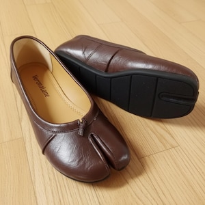 May include: A pair of dark brown split-toe flats with a smooth finish. The interior insole is light beige and features the brand name Veronalane printed in black. The shoes have a black rubber outsole with a distinct split design at the toe area.