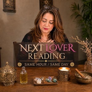 May include: A woman with long brown hair is seated behind a wooden sign that reads "NEXT LOVER READING." The table features a candle, crystals, a small bottle, and a decorative container. The overall theme is spiritual and mystical.