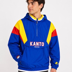 Peut inclure: Veste anorak Kanto Region bleue, jaune et rouge avec capuche et fermeture à demi-zip. La veste présente le mot "KANTO" en lettres blanches avec un contour rouge, et un logo de Poké Ball et d'étoile.