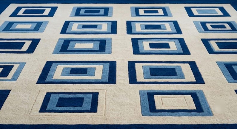 May include: A rectangular area rug featuring a repeating pattern of nested rectangles in shades of dark blue, light blue, and white. The design consists of multiple concentric rectangular frames arranged in a grid across a cream-colored background.