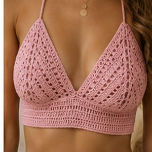 May include: A light pink crochet bralette featuring a triangular cup design with an intricate openwork pattern and a wide, solid-stitched band at the base. The garment includes thin, matching crochet straps that extend from the top of each cup.