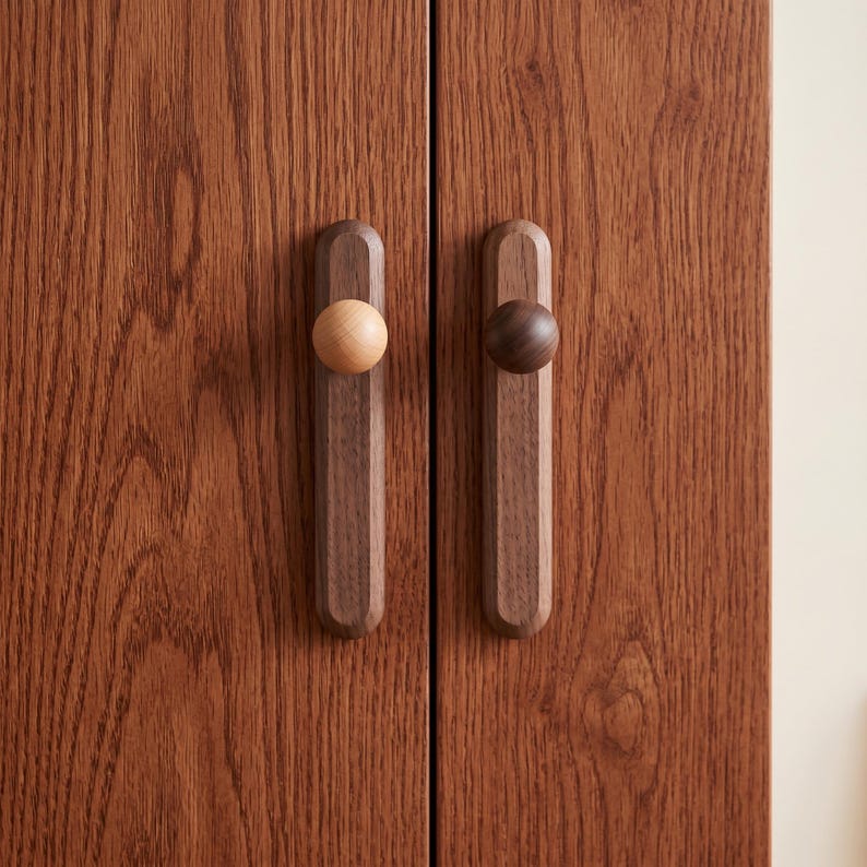 Puede incluir: Dos tiradores de armario verticales de madera montados en una puerta de madera de color marr&oacute;n rojizo con veteado. Cada tirador tiene una base rectangular larga con extremos redondeados y un pomo circular. Un pomo es beige claro y el otro marr&oacute;n.