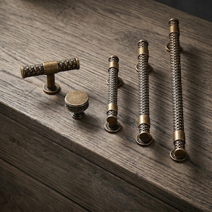 May include: A collection of five antique brass cabinet hardware pieces, including one T-bar pull, one round knob, and three bar pulls of varying lengths. Each piece features a textured, woven metal pattern and a dark, weathered finish.