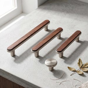 May include: Three cabinet pulls of varying lengths and one round cabinet knob. Each pull features a dark brown wood inlay set into a brushed silver metal frame. The round knob is made of solid brushed silver metal with a smooth, circular top.