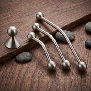 May include: A set of brushed silver metal hardware including one conical knob with a spherical top and three curved drawer pulls, each featuring spherical ends. The hardware has a smooth, matte finish and a consistent metallic silver color throughout.