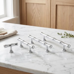 May include: Four polished chrome cabinet pulls arranged in a row, each featuring a segmented bamboo-inspired design. The hardware pieces vary in length, from a single-post knob to longer handles with two posts, all with a smooth, reflective finish.
