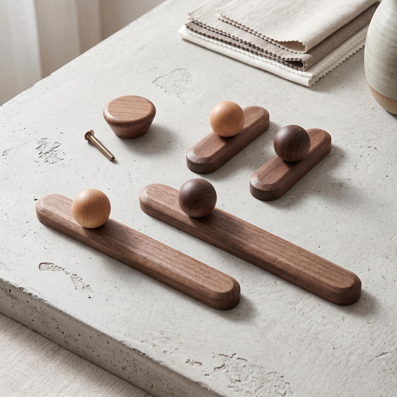 Puede incluir: Una colecci&oacute;n de herrajes de madera para muebles que incluye dos tiradores rectangulares largos con pomos esf&eacute;ricos, dos tiradores rectangulares m&aacute;s cortos con pomos esf&eacute;ricos, un pomo circular y un tornillo de metal. Tonos de madera claros y oscuros.