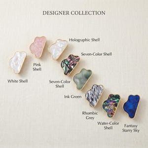 May include: A collection of nine irregular cloud-shaped cabinet knobs with gold-toned edges, labeled as Designer Collection. The set includes White Shell, Pink Shell, Holographic Shell, Seven-Color Shell, Ink Green, Rhombic Grey, Water-Color Shell, and Fantasy Starry Sky.