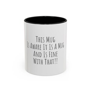 May include: White ceramic mug with a black interior and the text "THIS MUG IS AWARE IT IS A MUG AND IS FINE WITH THAT!!" printed in black. The mug is cylindrical and suitable for hot or cold beverages.