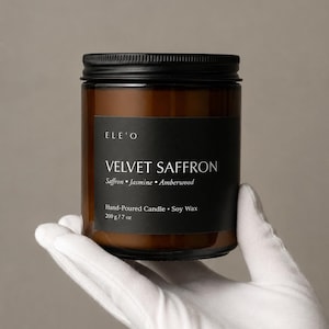 May include: A brown glass jar candle with a black lid and label. The label reads "VELVET SAFFRON" with scent notes and "Hand-Poured Candle • Soy Wax". The candle weighs 200 g.