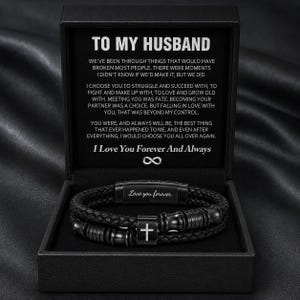 Puede incluir: Una pulsera trenzada negra con un dije de cruz central y detalles metálicos, presentada en una caja de regalo negra. La tapa incluye el texto TO MY HUSBAND seguido de un mensaje sentimental y la frase I Love You Forever And Always.