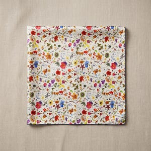 May include: A square fabric napkin featuring a dense, colorful botanical print on an off-white background. The pattern consists of various small, scattered wildflowers in shades of red, orange, yellow, purple, blue, and green, with thin stems.