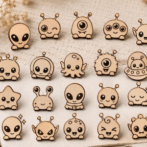 Könnte beinhalten: Eine Sammlung von neunzehn hellen Holz-Anstecknadeln mit verschiedenen Cartoon-artigen Alien-Figuren, Monstern und Himmelskörpern. Jedes kleine Holzstück zeigt eingravierte Gesichtszüge und deutliche Umrisse, die in einem Raster angeordnet sind.