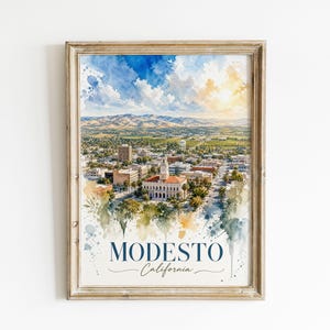 Può includere: Una stampa ad acquerello incorniciata del paesaggio urbano di Modesto, California, con un edificio centrale con torre dell'orologio, strutture urbane circostanti e montagne in lontananza sotto un cielo luminoso. Il testo MODESTO California è in basso.