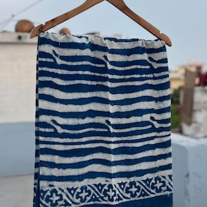 Peut inclure: Une pièce textile rectangulaire présentant un motif de rayures horizontales ondulées bleu foncé et blanc cassé. Le tissu affiche une bordure distincte en bas avec un motif géométrique répétitif en forme d'étoile, le tout en style batik.