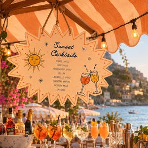 May include: A starburst-shaped wooden sign hanging under a striped awning, featuring the text Sunset Cocktails, a sun illustration, and a list of drinks including Aperol Spritz, Hugo Spritz, Passion Fruit Spritz, Bellini, Limoncello Spritz, and Gin Tonic.