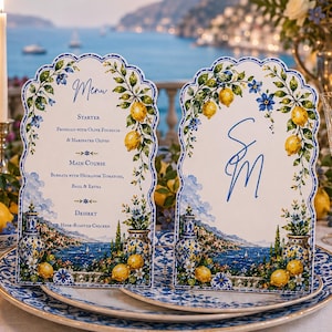 May include: Two arched menu cards featuring a watercolor illustration of lemons, blue flowers, and coastal scenery. The left card displays the word Menu and food courses, while the right card features the blue monogram letters SM in a script font.