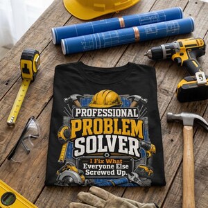 Könnte beinhalten: Ein schwarzes T-Shirt mit einer Grafik aus gelbem Schutzhelm, Hämmern, Bohrmaschine und Bauplänen sowie dem Text "PROFESSIONAL PROBLEM SOLVER I Fix What Everyone Else Screwed Up." Das T-Shirt ist von verschiedenen Bauwerkzeugen umgeben.