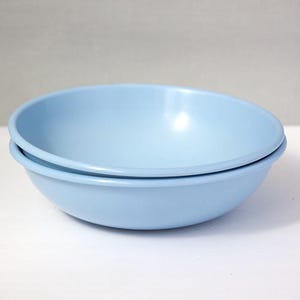 May include: Two light blue bowls stacked on top of each other. The bowls are round with a slightly flared rim. The bowls are made of a solid, opaque material and are a soft, pastel blue color. The bowls are sitting on a white surface.
