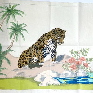 May include: A hand-painted illustration of a jaguar sitting on a rock, surrounded by palm trees, flowers, and a small pond. The jaguar has a tan coat with black spots. The scene is set in a tropical environment.