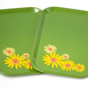 May include: Two green rectangular trays with rounded corners. Each tray features a cluster of yellow and orange daisies in the corner. The trays are likely made of metal or a similar material.