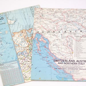 May include: Two vintage National Geographic Magazine maps. One map shows the world, with a blue ocean and landmasses in shades of green, brown, and yellow. The other map focuses on Switzerland, Austria, and Northern Italy, with detailed geographical features.
