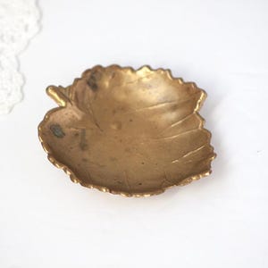 May include: A vintage brass leaf-shaped dish. The dish has a detailed leaf vein pattern and a slightly tarnished, golden finish. It is a decorative item, suitable for holding small items or as a display piece.