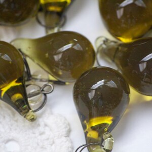 K&ouml;nnte beinhalten: Eine Sammlung olivgr&uuml;ner, tropfenf&ouml;rmiger Glasornamente. Jedes Ornament hat eine kleine Metallschlaufe zum Aufh&auml;ngen. Das Glas hat einen leichten Gelbstich und reflektiert das Licht. Die Ornamente sind wahrscheinlich f&uuml;r dekorative Zwecke.