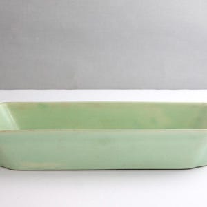 May include: A rectangular, light green ceramic baking dish. The dish has a slightly scalloped edge and a rectangular shape. The color is a soft, muted green, and the dish appears to be vintage or antique.
