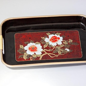 May include: Rectangular black tray with a gold rim and woven handles. The tray features a red and black floral design with white and red flowers and gold accents. A decorative serving piece.