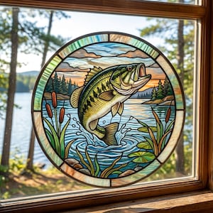 May include: A circular stained glass panel featuring a green and gold bass fish jumping out of blue water. The scene includes brown cattails, green lily pads, and a background of pine trees under a sunset sky, all framed by a decorative glass border.
