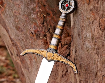 May include: A decorative sword featuring a silver and gold-toned hilt with intricate floral engravings on the crossguard. The pommel is circular with a central red stone inlay. The blade is metallic silver with a visible etched emblem near the hilt.