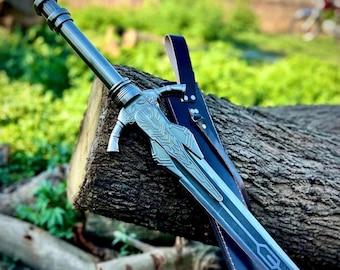 May include: A silver-toned metal sword featuring an intricate, embossed design on the crossguard and a long, straight blade. The sword is accompanied by a dark-colored leather scabbard with visible stitching and metal hardware attachments.