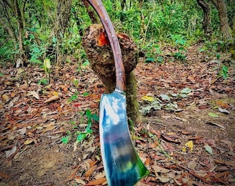 May include: A large, curved metal blade with a polished, reflective surface and a long, smooth wooden handle. The blade features a wide, sweeping edge that tapers toward the base, while the handle is secured with visible metal rivets.