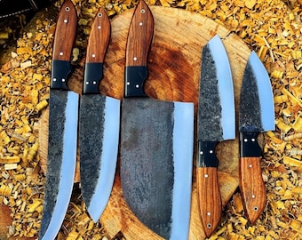 May include: A set of five kitchen knives with dark, textured metal blades and polished wooden handles secured by three silver rivets. The knives vary in size and shape, including a large cleaver and several pointed blades, arranged on a wooden surface.