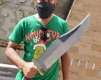 May include: A large, fixed-blade knife with a textured, dark metal finish on the upper portion of the blade and a smooth, polished edge. The handle is made of dark, textured antler material, featuring a brass-colored bolster and pommel cap.