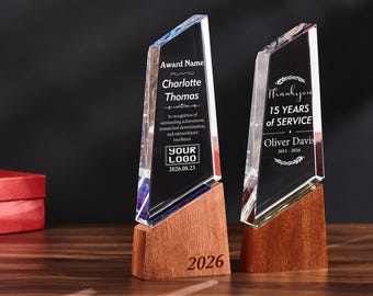 May include: Two clear, angled crystal awards mounted on rectangular wooden bases. The left award features the text 'Award Name', 'Charlotte Thomas', and 'YOUR LOGO'. The right award displays 'Thankyou', '15 YEARS of SERVICE', and 'Oliver Davis 2011-2026'.