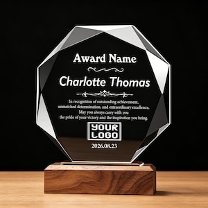 May include: An octagonal black glass award plaque with beveled edges, mounted on a rectangular wooden base. The glass features white engraved text reading Award Name, Charlotte Thomas, and a placeholder for a logo above the date 2026.08.23.