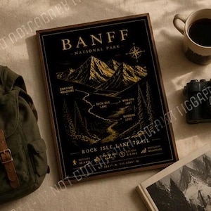 Peut inclure: Une impression encadrée rectangulaire sur fond noir avec des illustrations dorées du parc national de Banff et du sentier Rock Isle Lake. Le design comprend des sommets montagneux, un sentier sinueux, des silhouettes de forêt et une rose des vents.