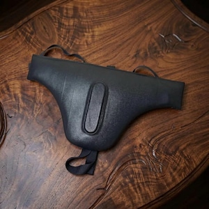 May include: A black protective athletic cup with a molded, contoured shape and a central vertical ridge. The item features integrated black elastic straps at the top and bottom, designed for secure positioning during physical activity.