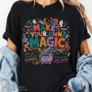 May include: A black t-shirt featuring a colorful graphic with the text "MAKE YOUR OWN MAGIC," "stir up something wonderful," and "believe in your spark." The design includes a purple cauldron, ghosts, bats, stars, crystals, and swirling smoke.